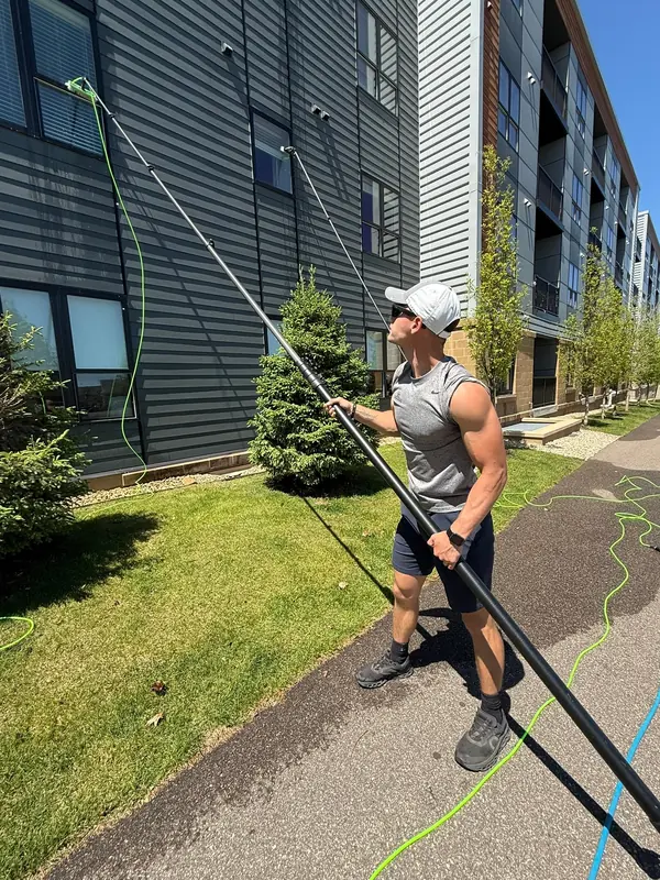 Technician working a water-fed pole along an apartment building