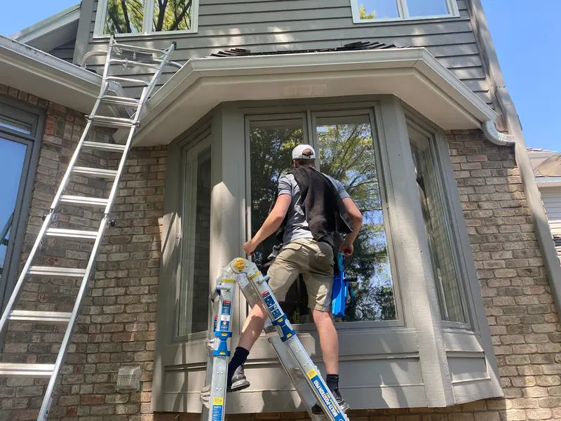 Cleaning a bay window from a ladder on a brick home