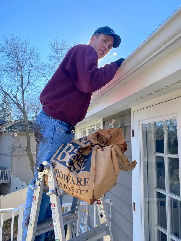 Technician cleaning gutters from a ladder