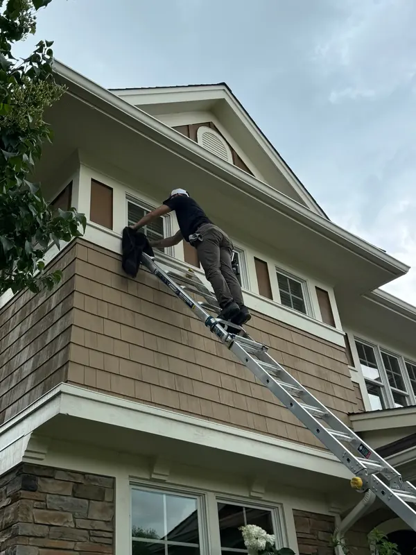 Technician on an extension ladder cleaning the upper windows of a large home