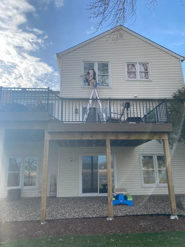 Technician on a ladder cleaning the upper windows of a two-story home