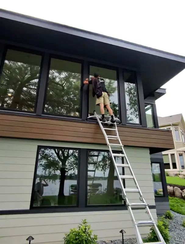 Cleaning the high windows of a modern home from a ladder