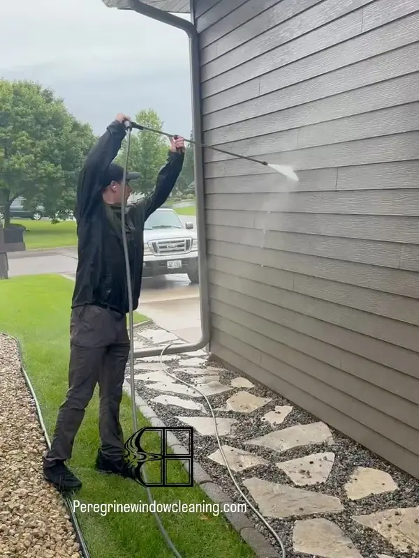 Pressure washing the siding of a home beside a stone path