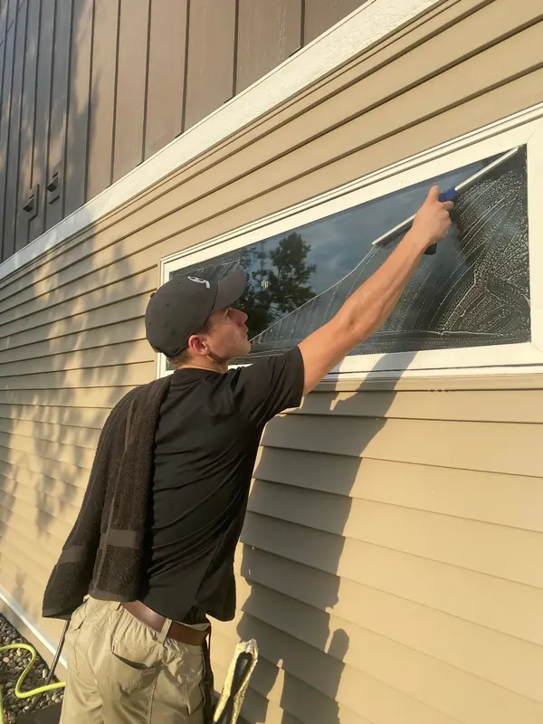 Squeegeeing a long window on a tan-sided home