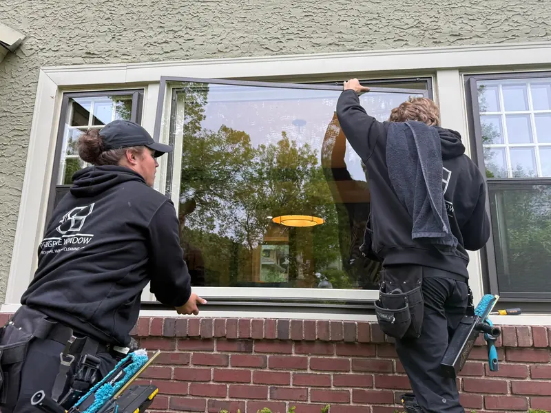 Two technicians cleaning a large window on a brick building