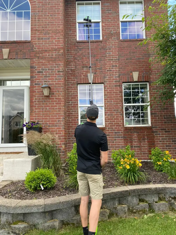 Cleaning second-floor windows on a brick home with a water-fed pole